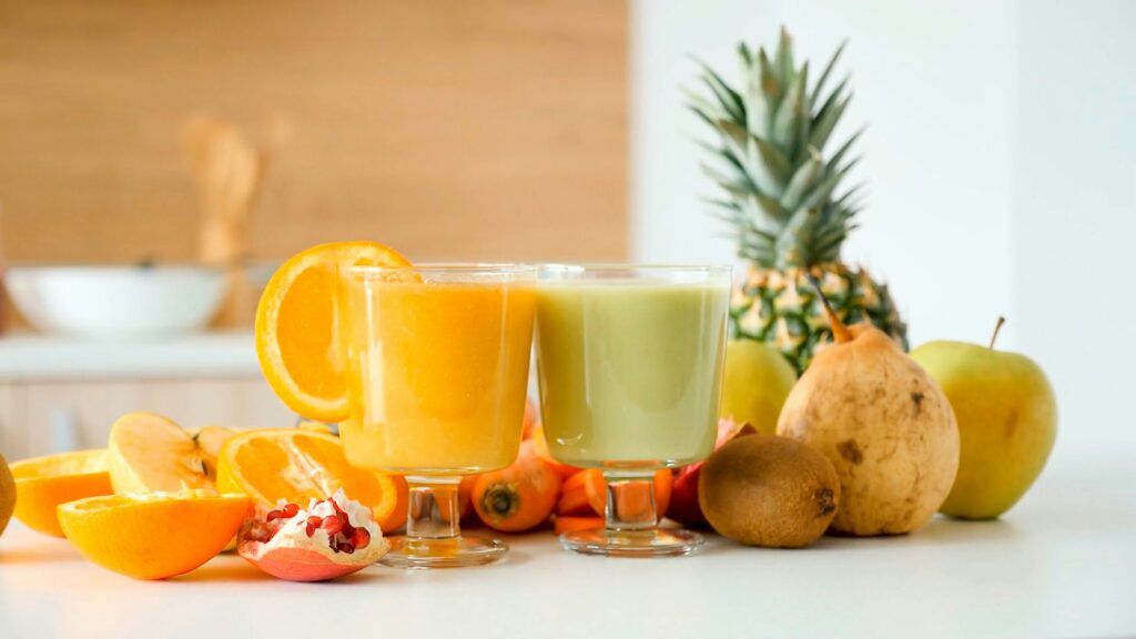Green and orange smoothie with fruit on a table