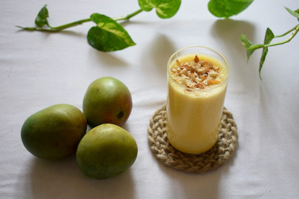 Mango smoothie in glass with 3 mangos on the side